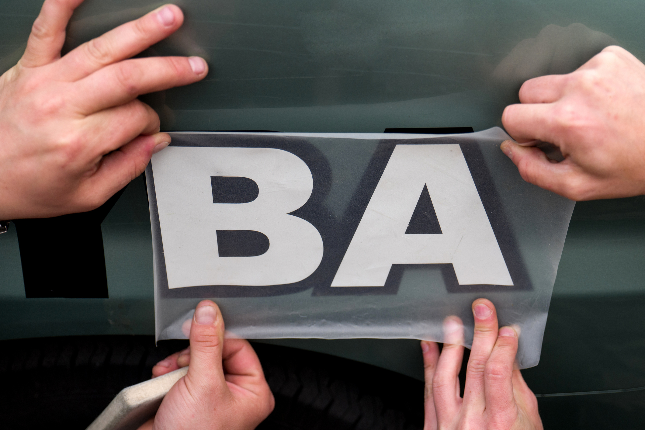 Hands applying a finished cut-vinyl decal to a vehicle panel