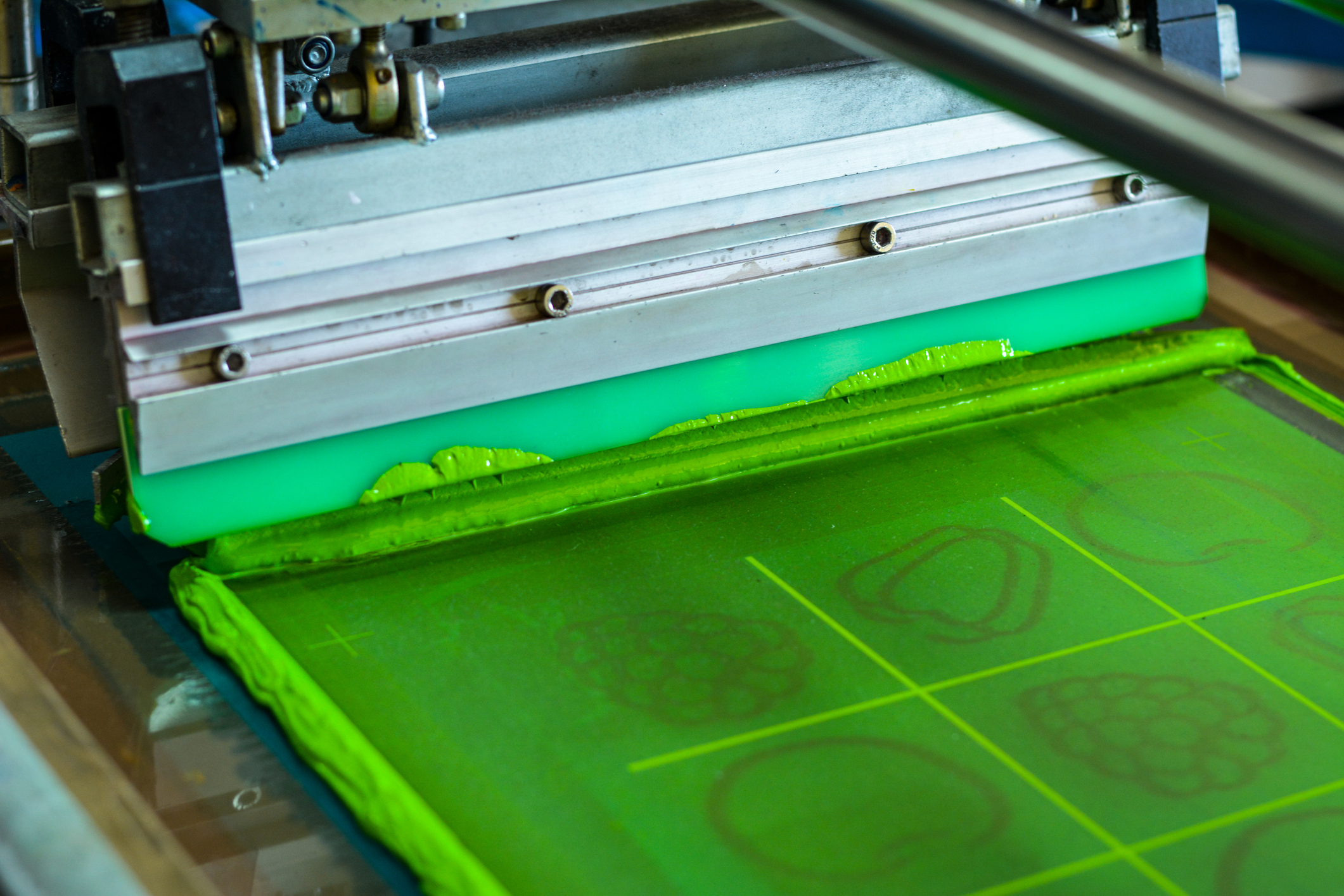 Screen printing press laying down green ink on a screen mid-run